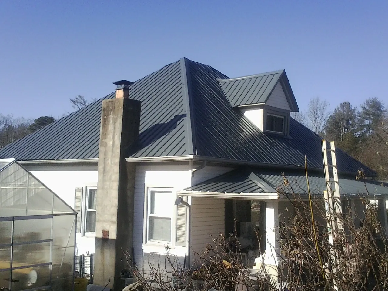 Dark blue standing seam metal roof on a white farmhouse with dormer — Slate & Tile Roof Repair by Roofing Brothers in Housatonic