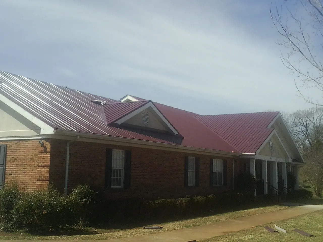 Red metal roof with gabled entries on a long brick building, from a Hail Damage Roof Repair job in Housatonic