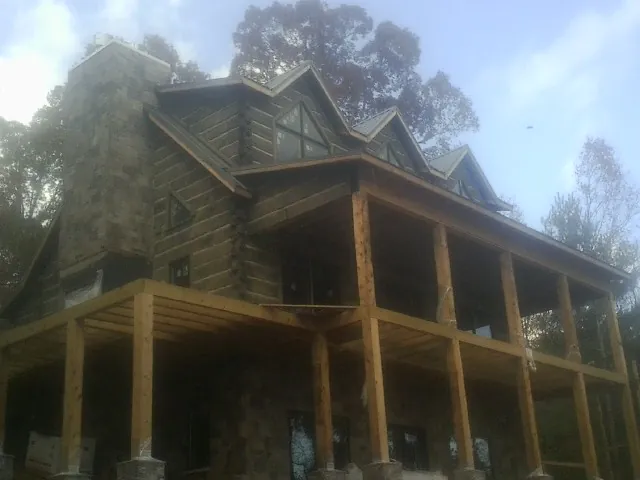 Stone chimney and dormers on a large log home with a timber porch in Housatonic
