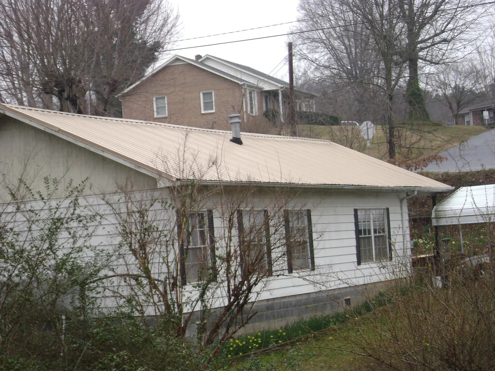 Tan metal roof on a white sided house set into a hillside — Commercial Roofing by Roofing Brothers in Housatonic